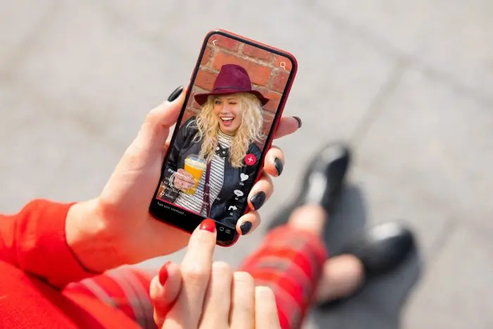 Smiling woman holding a smartphone showing a short video of herself with a drink