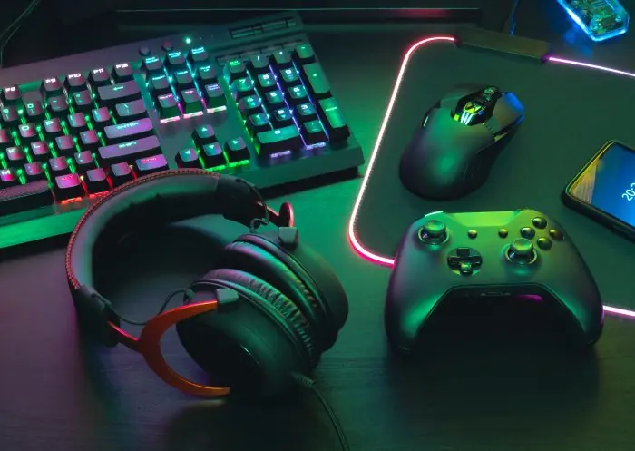 Gaming setup with a backlit keyboard, mouse, controller, headset and smartphone on a glowing RGB desk mat