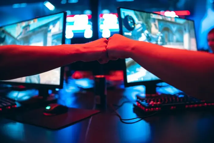 Two gamers fist-bumping in front of monitors in a dim room lit red and blue