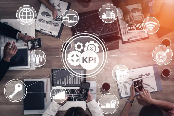 Overhead view of team at a desk with a glowing KPI gear icon and analytics symbols