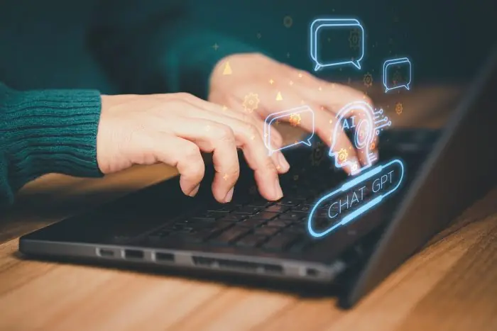 Hands typing on a laptop with glowing ChatGPT and chat bubble icons floating above the keyboard