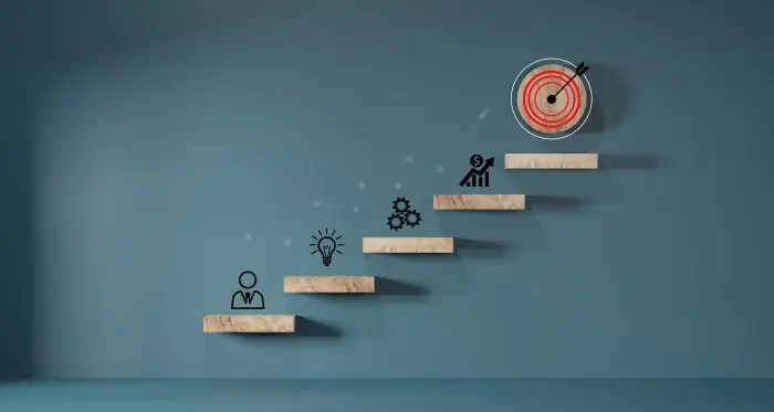 Wooden steps with icons rising from person to idea, gears, growth and a target, representing paid media goals