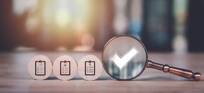 Magnifying glass with a checkmark beside three wooden tokens showing clipboard icons