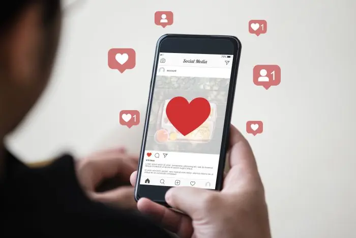 Hand holding a smartphone showing a social media feed with floating heart and follower notification icons
