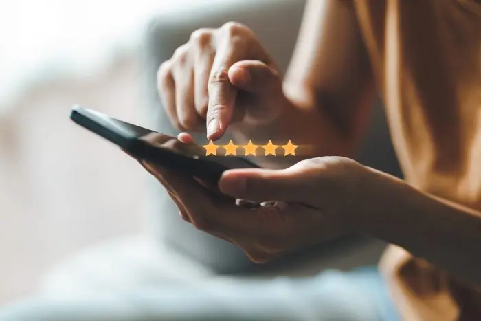 Hand tapping a smartphone with five gold rating stars above the screen