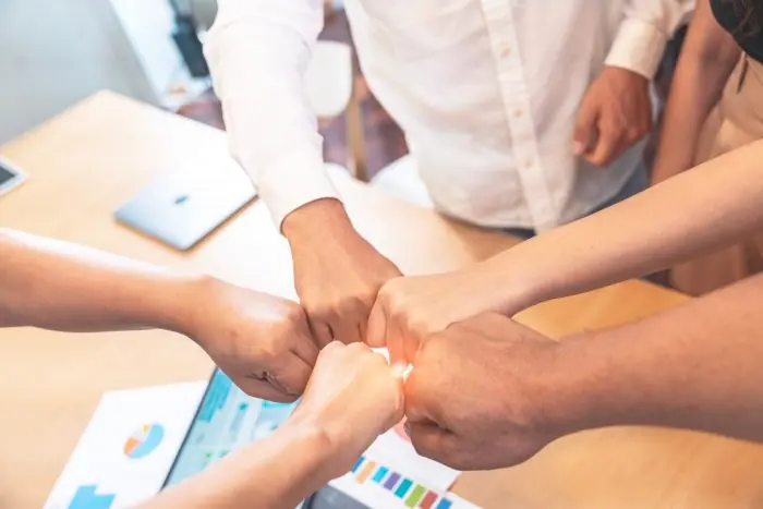 Team joining fists together over a desk with printed charts, symbolizing business collaboration