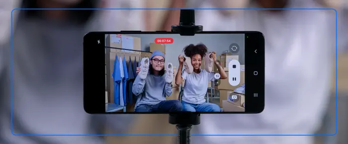 Two people holding sneakers in front of a smartphone on a tripod recording a live video